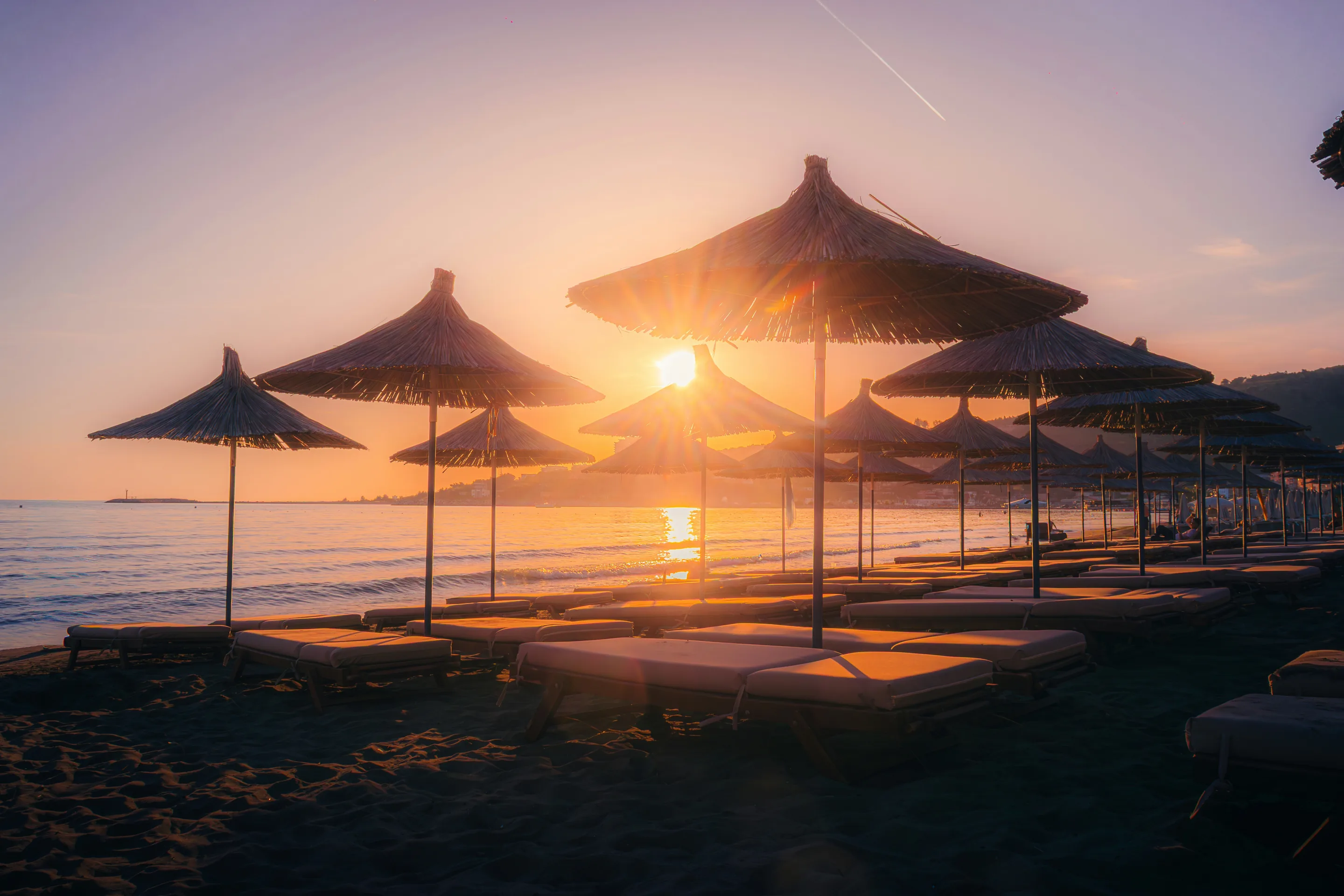 Straw parasols and loungers against the sun setting over a calm sea