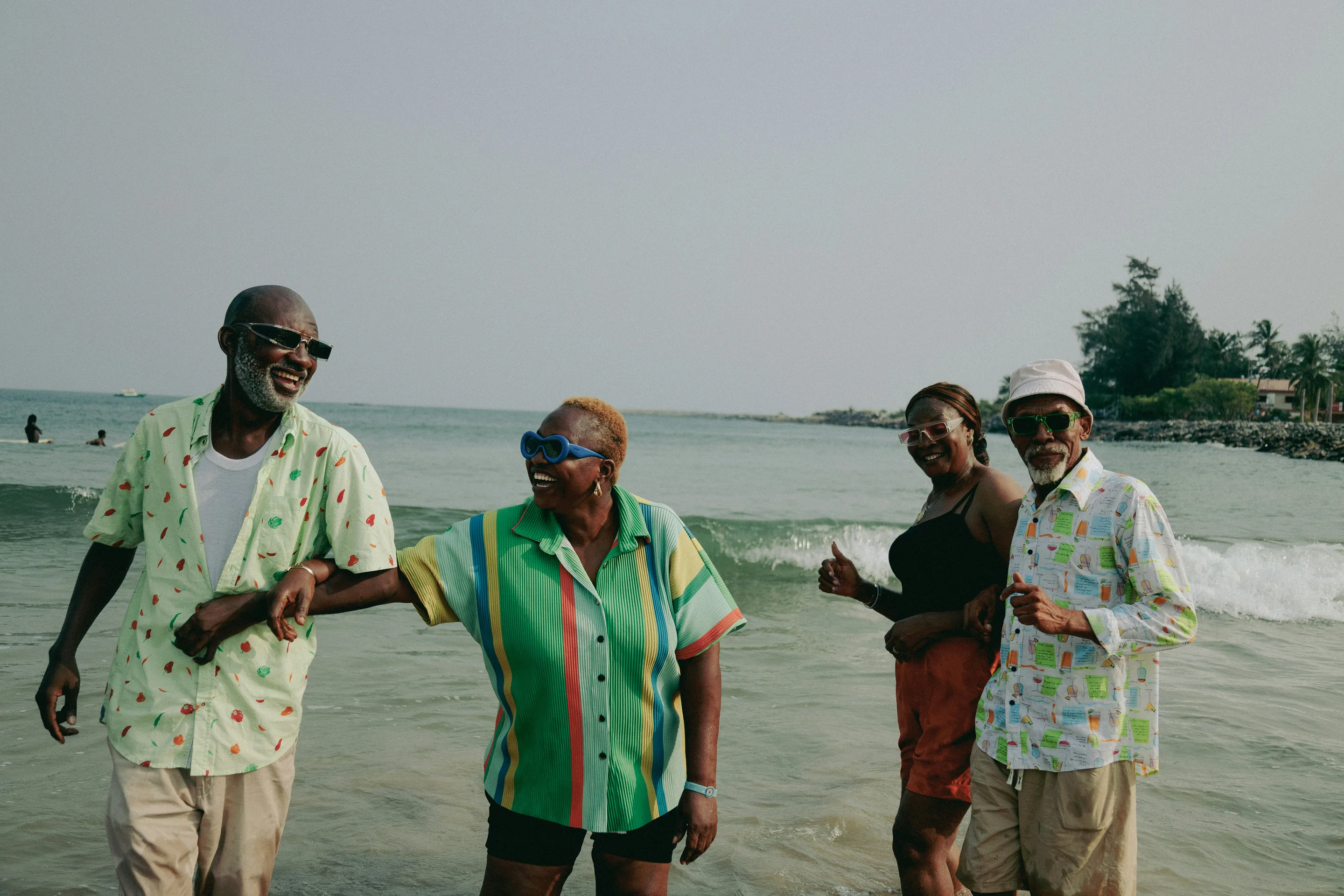 Friends in bright print shirts laughing and dancing in the surf